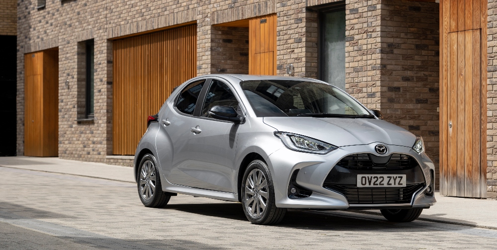 Mazda 2 hybrid driving past a garage