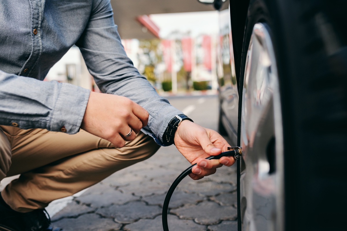 Close up of man crouching on the gas station and inflating tyre